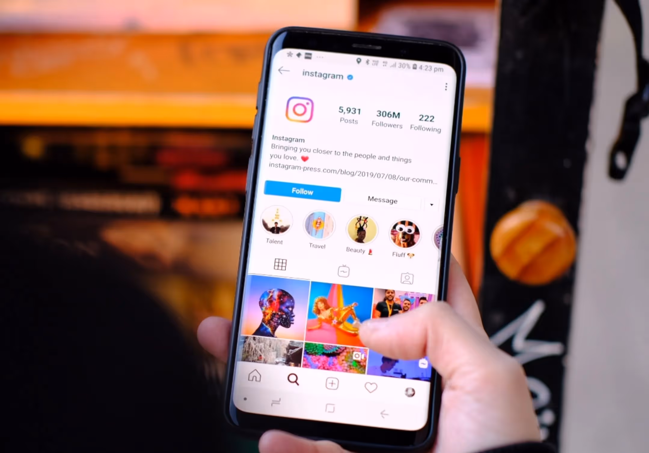 A hand holding a phone showing an Instagram profile page and its grid of posts