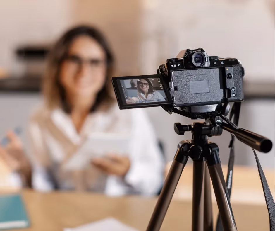 Camera on a tripod filming a woman holding notes, her face visible on the flip-out screen