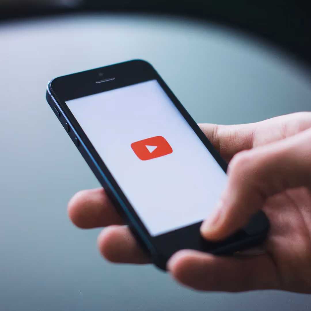 A hand holding a phone that shows the red YouTube play logo on a white screen