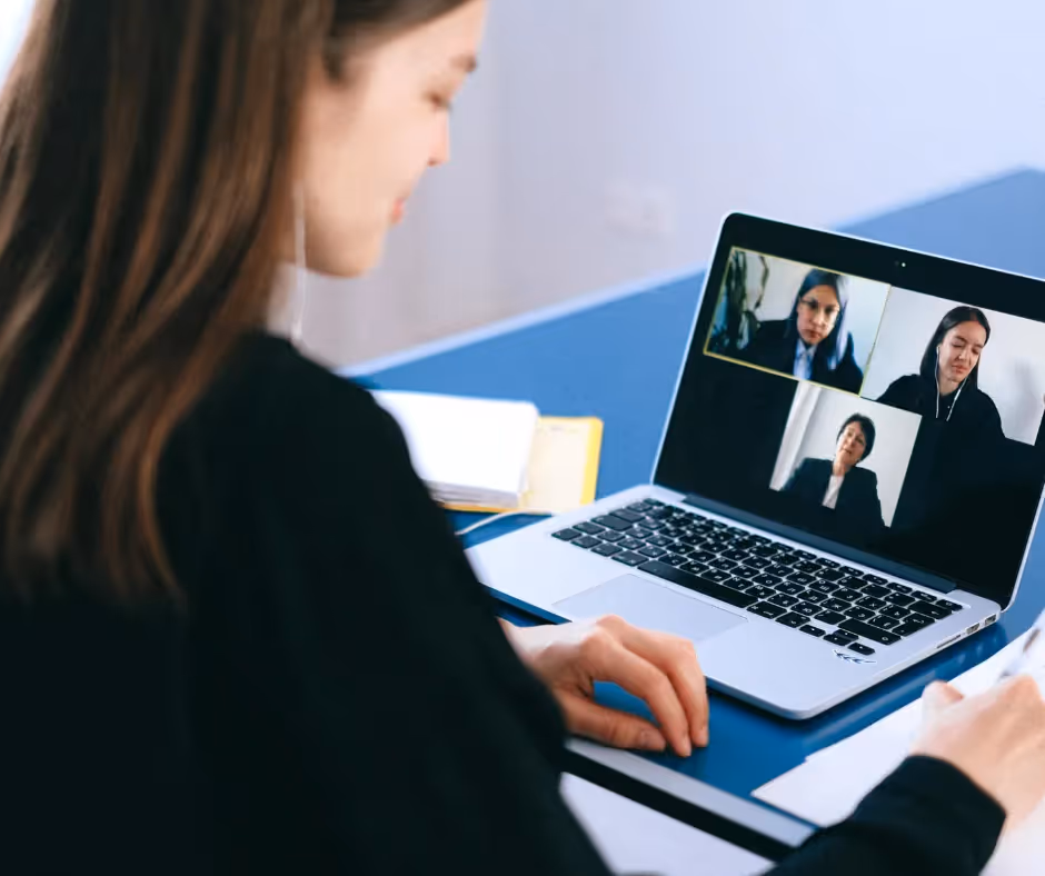 Woman at a laptop on a video call, three participants visible in the on-screen grid