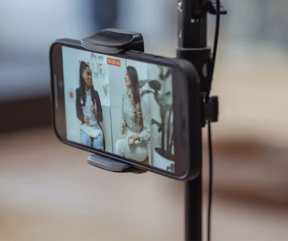 A phone clamped to a tripod filming two women in conversation, recording timer running on screen