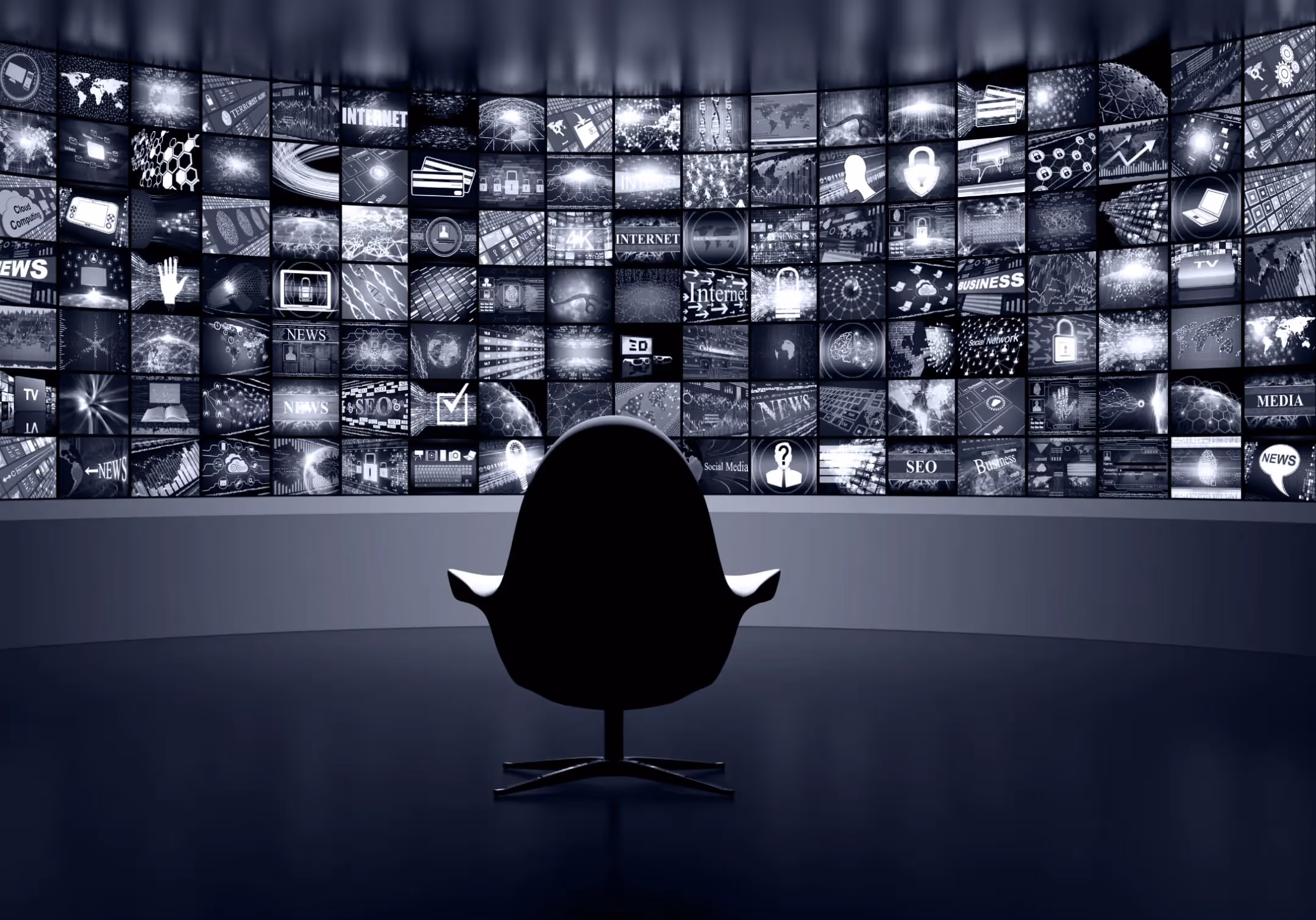An empty chair facing a curved wall of dozens of screens showing news and media imagery