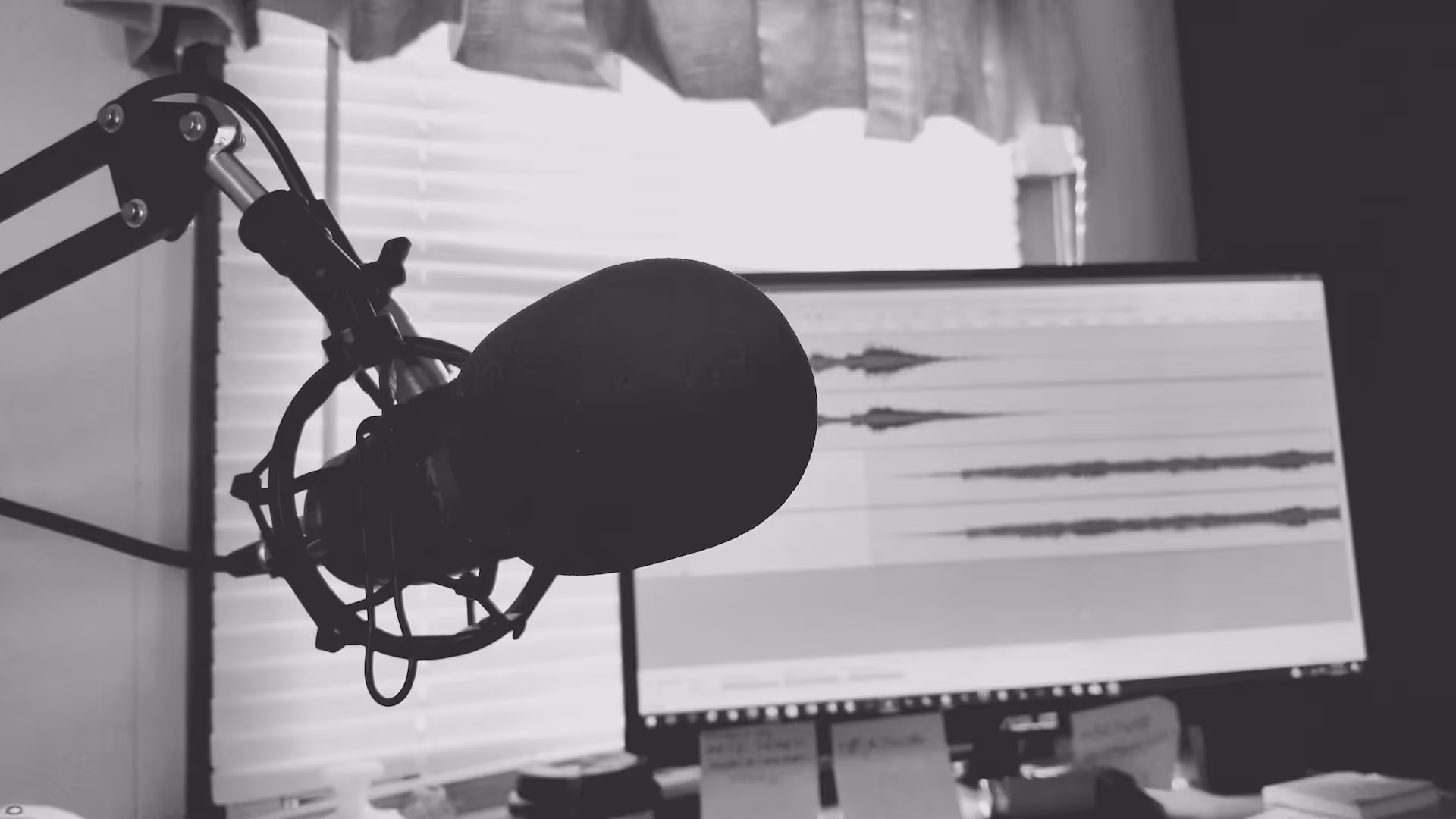 Black and white photo of a studio microphone on a boom arm in front of an audio waveform on screen