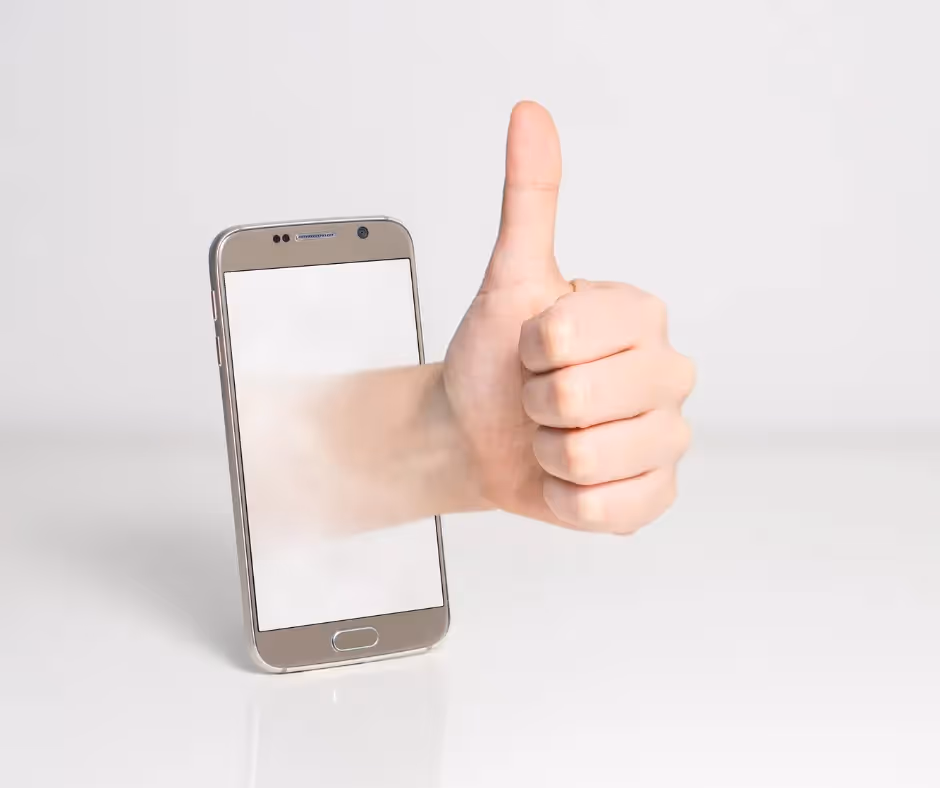 A hand giving a thumbs-up reaching out through the blank screen of a smartphone