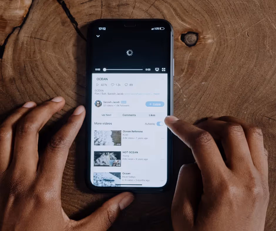 Two hands holding a phone playing a video, resting on a wooden table